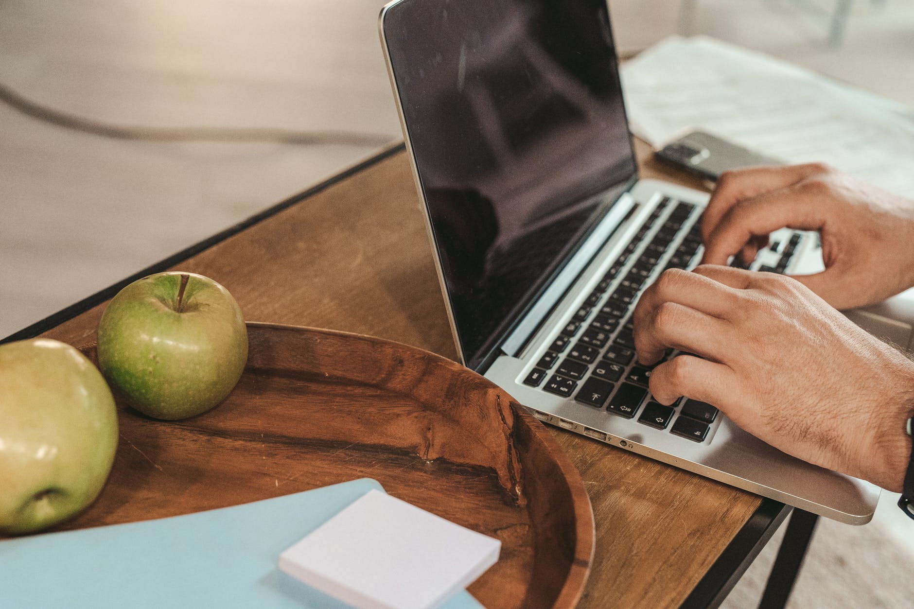 person using a silver laptop on brown wooden table
